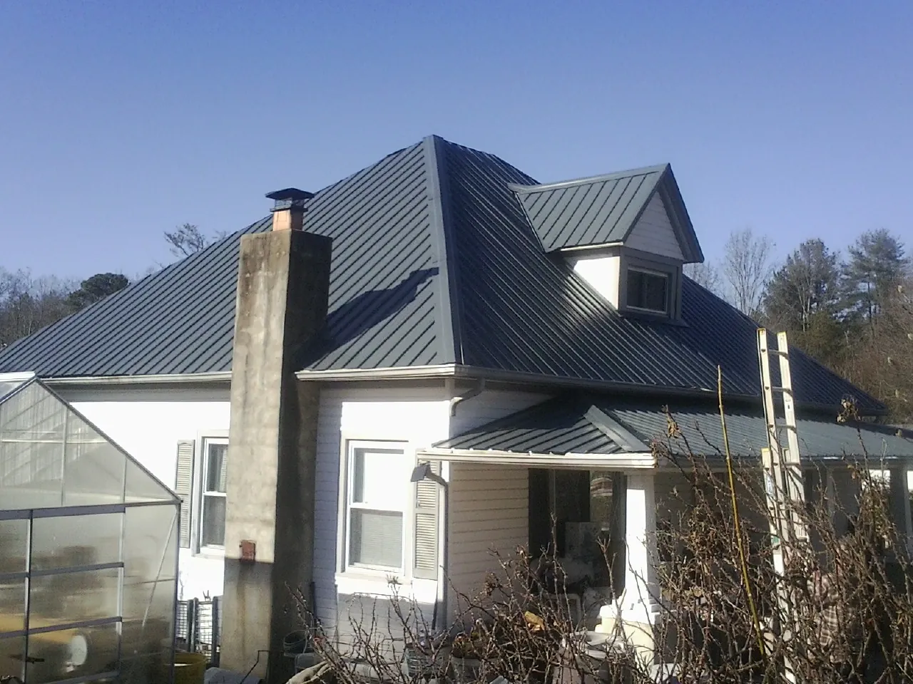 Dark blue standing seam metal roof on a white farmhouse with dormer — Slate & Tile Roof Repair by Roofing Brothers in Piffard