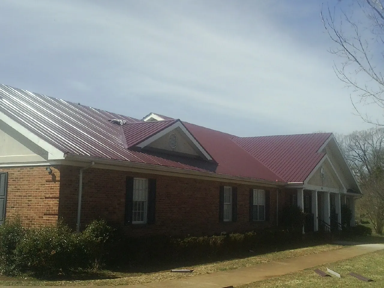 Red metal roof with gabled entries on a long brick building, from a Hail Damage Roof Repair job in Piffard