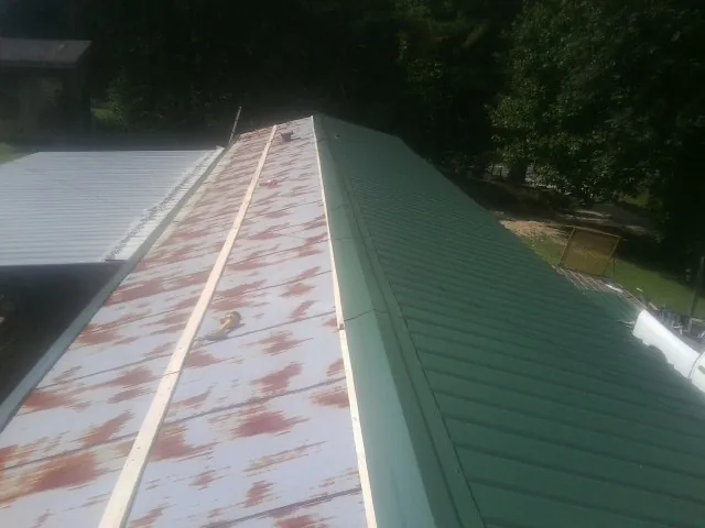 Old rusted panels beside newly installed green metal roofing — Wind Damage Roof Repair by Roofing Brothers in Piffard