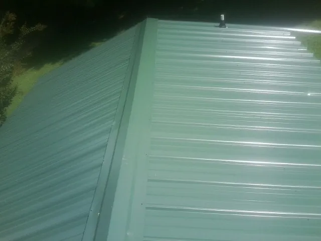 New green metal panels meeting at the ridge of a roof — Flat Roof Repair work by our crew in Piffard