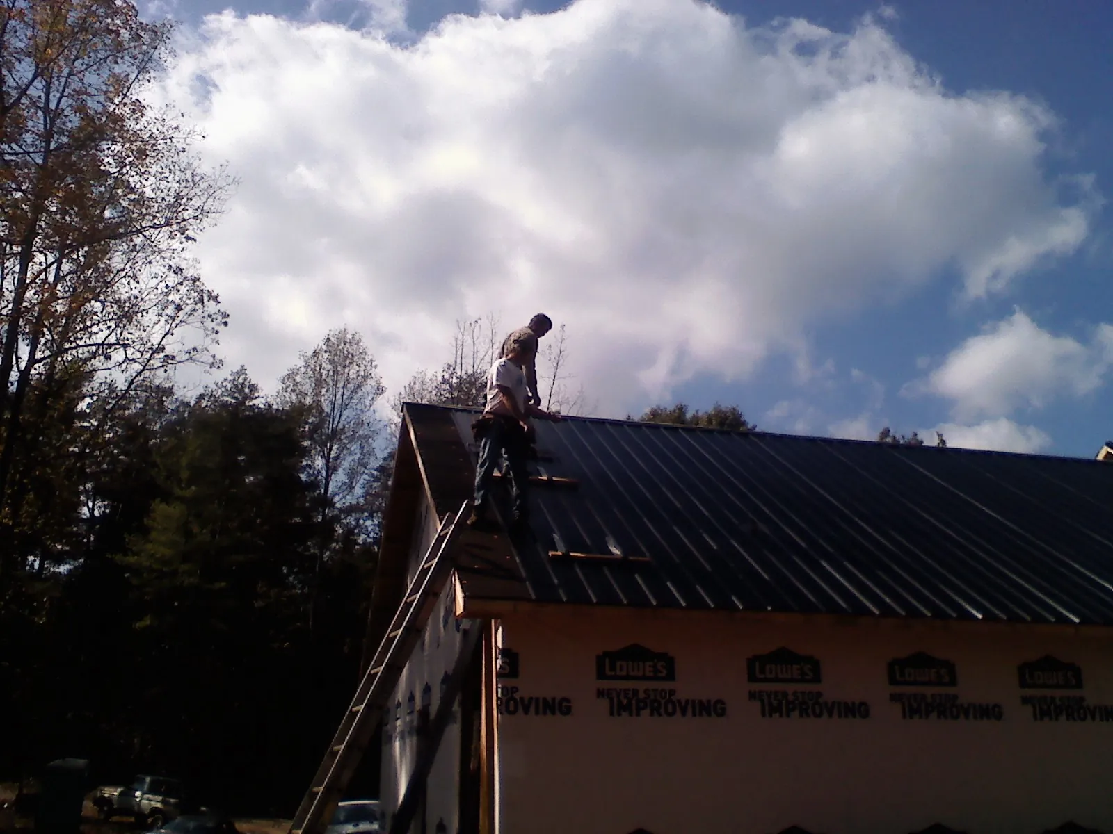 Roofer fastening dark metal panels high against a cloudy sky, from a Roof Inspection job in Piffard