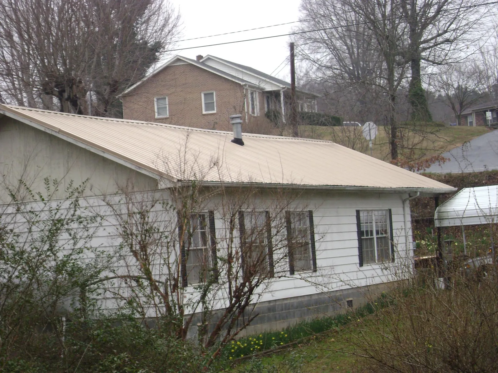 Tan metal roof on a white sided house set into a hillside — Commercial Roofing by Roofing Brothers in Piffard