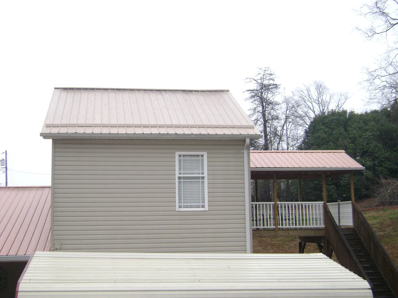 Tan metal roofs on a two story addition and attached porch, from a Roof Replacement job in Piffard